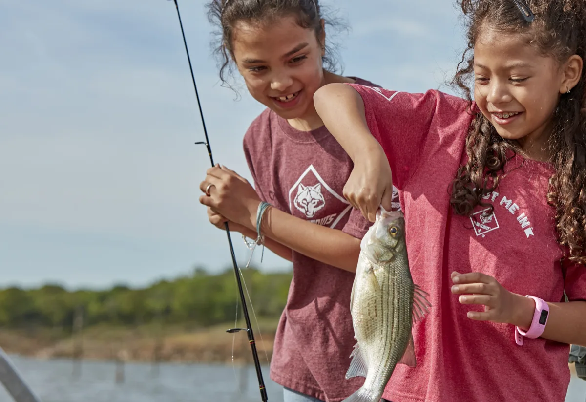 Two Cub Scout girls excitedly holding up a fish they caught together